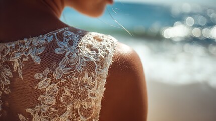 A bride in a lace dress stands on a beach with the ocean in the background on a sunny day scene