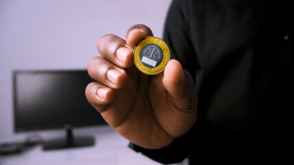 Black African person in black shirt holding showing pointing single one 1 Ghanaian cedi coin in a room. close up of Hand holding coin