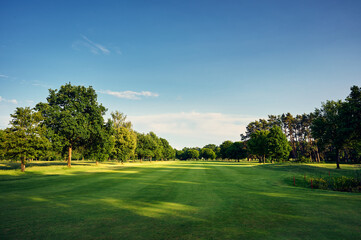Scenic view of a green golf fairway lined with trees under a clear blue sky. Ideal for outdoor, sport, and leisure themes.