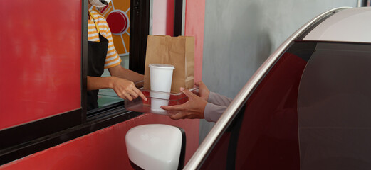 A customer picks up a French fries burger from a drive-thru counter employee during rush hour.