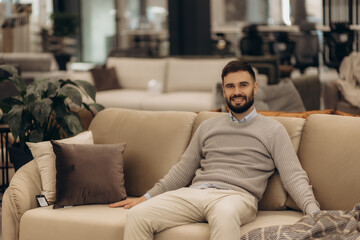 Obraz premium Young Man Relaxing on Stylish Sofa in a Modern Furniture Store