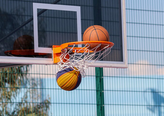 A basketball is stuck in a net with a yellow and blue ball in the net