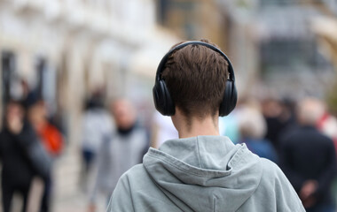 A man wearing headphones is walking down a street with a group of people © schankz