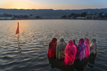on Chath Pooja Women offering prayers to Lord Sun standing in water of Pushkar Lake with a beautiful sunrise view