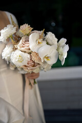 young girl in a white wedding dress holds in her hands a bouquet of flowers and greenery 