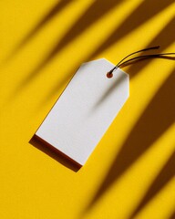 A white blank price tag with a string lies on a bright yellow background with light shadows.