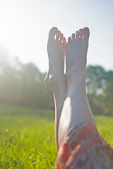 Summer Holidays Concept. Legs of Young Caucasian Female Against Sunny Sky and Green Grass Field