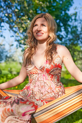 Relaxed Resting Young Winsome Caucasian Blond Sexy Female Posing in Hammock Outdoors Over Green Field Background