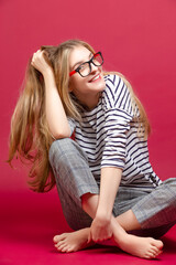 One Happy Winsome Excited Energetic Girl Sitting on Floor With Glasses And Making Faces on Crimson Background.