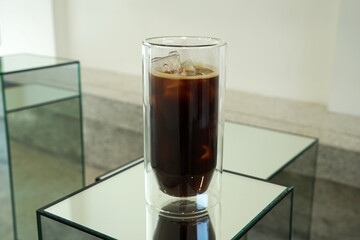 Close up double wall glass of iced black Americano coffee on mirror stool table