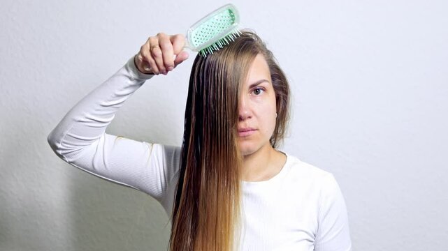 Pretty young woman combing her long hair. Woman combing her wet hair with a brush. Clean long washed female hair.