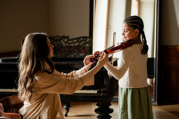 teacher teaches a girl to play the violin in class.