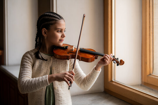 A young girl with braided hair skillfully plays the violin.
