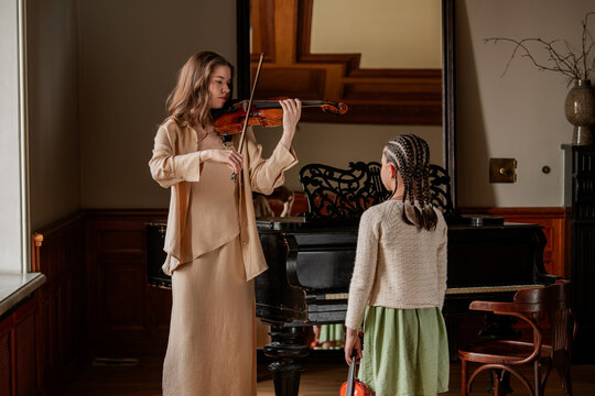 Woman playing violin for young girl in music class