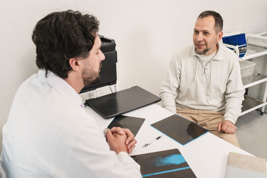 reception consultation doctor patient in the clinic in the office of a traumatologist orthopedist. Rehabilitation after injury. Doctor looks at an x-ray with a patient sitting at the table