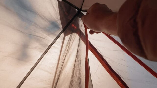 Point-of-view shot from inside a camping tent showing a hiker unzipping and zipping the entrance flap to glance at the surrounding nature.