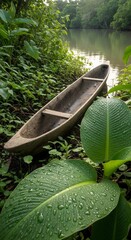 Tranquil River Scene: Dugout Canoe Resting by Lush Green Rainforest Riverbank