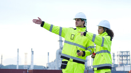 Industrial Engineers Discussing Plans at a Refinery Site, Two Safety-Clad Workers Pointing and Collaborating at an Industrial Facility, Teamwork and Supervision at an Outdoor Chemical Plant