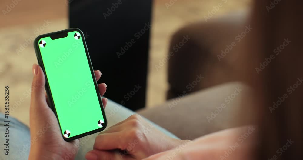 Wall mural female using smartphone with green screen mock up display at home. browsing the internet and checkin