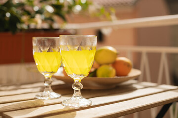 Glasses with refreshing citrus lemonade and a plate of fresh citrus fruits on the table on the sunny balcony.
