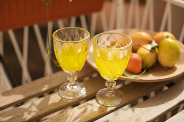 Glasses with Italian lemon liqueur and a plate of fresh citrus fruits on the table on the sunny balcony.