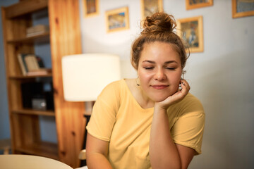 Early wake up, insomnia, lack of sleep. Sleepy woman in casual home clothes trying to wake up and start working from home on laptop sitting at table in her living-room, holding her cheek with hand