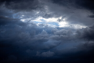 The photo shows a dark stormy sky with dense clouds. Faint light breaks through the thick cloud cover, creating a contrast between the bright and dark areas of the sky.