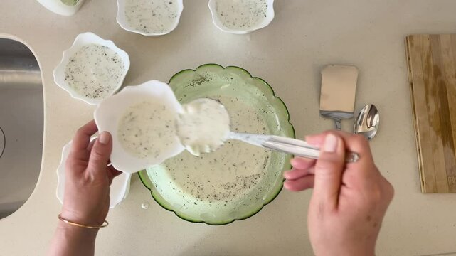 The woman is serving cacik, made with cucumber and yogurt in the Turkish style, in bowls at the dining table.