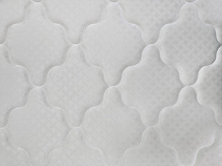 A close-up view of a white quilted mattress surface with geometric stitching and padded texture, showcasing textile detail and comfort design.
