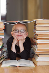 A child lies between tall stacks of books, holding one open and balancing another like a roof...