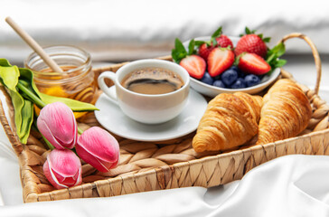 Romantic breakfast in bed with coffee, croissants, berries, honey and tulips