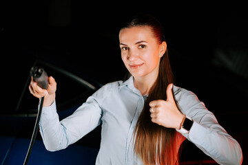 Woman plugs in electric car charger in underground parking lot during evening hours