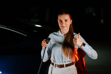 Woman charging electric vehicle in underground parking facility at night