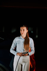 Woman charging electric vehicle in underground parking facility during evening hours