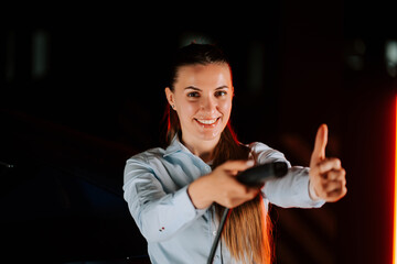 Woman charges electric car in underground parking lot while smiling and giving thumbs up