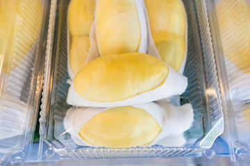 Close-up of durian fruit neatly packed in a clear plastic container, showcasing bright yellow flesh and white edible seeds