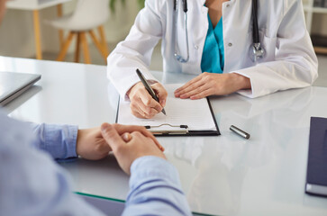 Female doctor, general practitioner filling paper medical records consulting patient in clinic, GP...