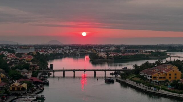 Drone view of Hoi An, Vietnam in the early morning showing the beautiful sunrise. Boats float on the Thu Bon River beside yellow historic buildings . Peaceful and scenic.