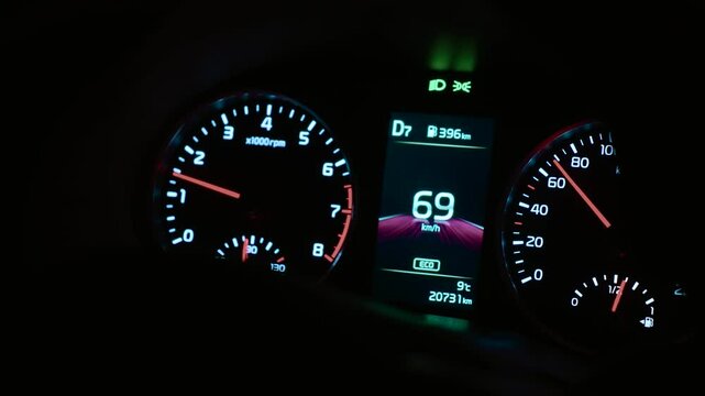 Car dashboard with analog dials indicating speed, engine RPM, fuel range, gear, and ECO mode. Instrument panel showing current velocity and driving stats under night lighting. Display presenting