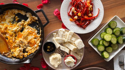 Turkish breakfast served on a wooden table. Cheese, cucumber slices, omelet, and fried red pepper slices.