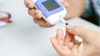Person using blood glucose meter to check blood sugar level, close up of hand holding device and...