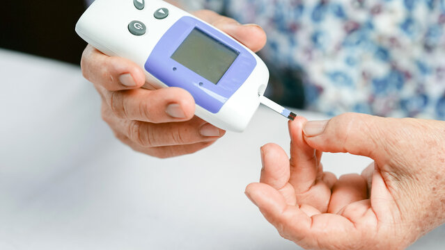 Blood glucose meter diabetes test elderly hand checking blood sugar healthcare medical device monitoring finger prick close up home test health awareness.