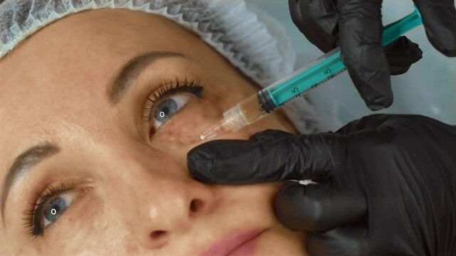 Cosmetologist injecting filler into under-eye area of woman for rejuvenating facial procedure. Aesthetic doctor performing tightening and wrinkle-smoothing treatment in beauty clinic. Beautician