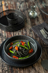 Black spaghetti with asparagus and dried tomatoes served on black plate