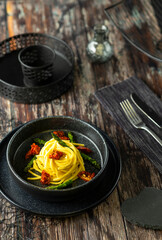 Delicious spaghetti with asparagus and dried tomatoes served on black ceramic plate