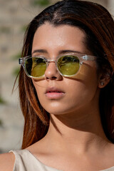 Young woman with long brown hair wearing stylish sunglasses and casual clothing, enjoying a sunny day outdoors