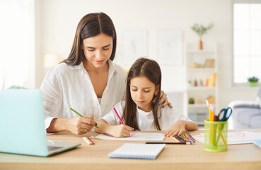 Obraz premium Mother and child doing school homework together. Little girl together with mom sitting at desk and drawing picture with colored pencils. Family, education concept