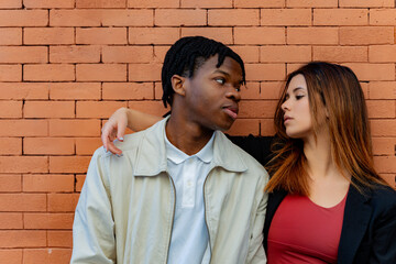 Young multi ethnic couple embracing and gazing into each other's eyes, surrounded by a stylish brick wall that enhances their connection