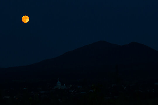 Full moon floats over distant mountains and a quiet village, radiating calm and mystery under a starless sky