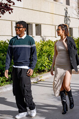 Young man and woman, likely colleagues, are walking and talking on a sidewalk outside their office building during a work break